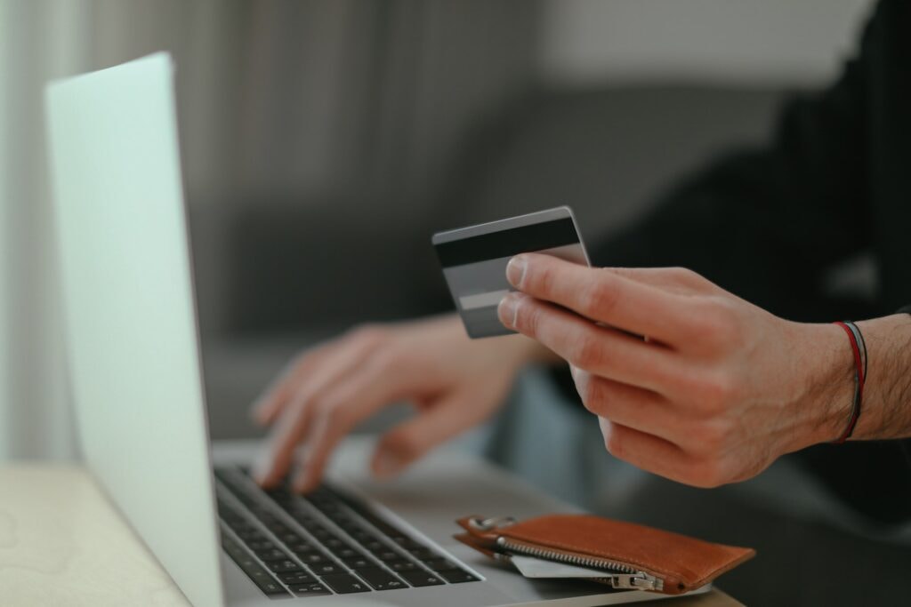 Person hält Kreditkarte in der Hand und gibt Daten im Laptop ein.